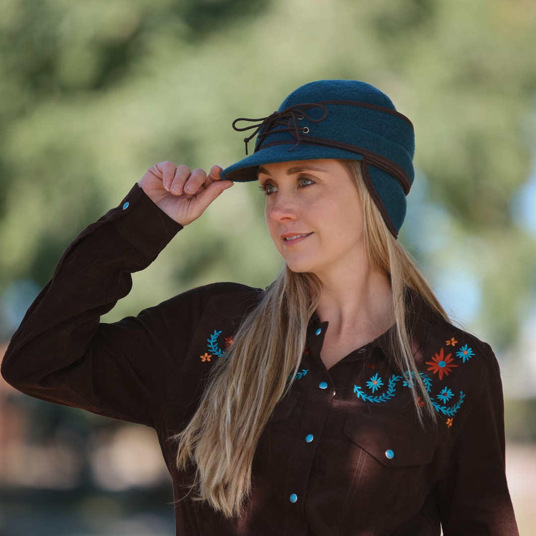 Amber Marshall from Heartland wearing a brown embroidered shirt and the Amber Marshall signature blue hat by Crown Cap outdoors