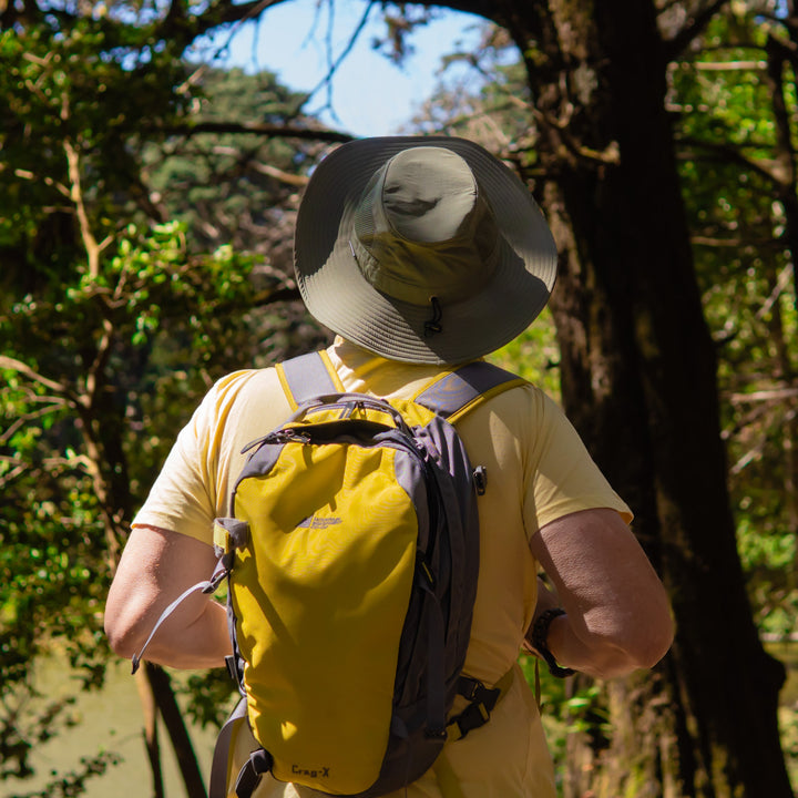Person wearing a yellow shirt and brown pants with a backpack, standing in a forest.