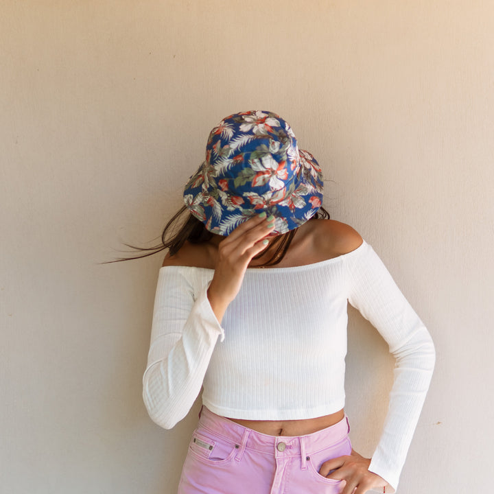 Person wearing a floral headscarf and white long-sleeve top against a plain background