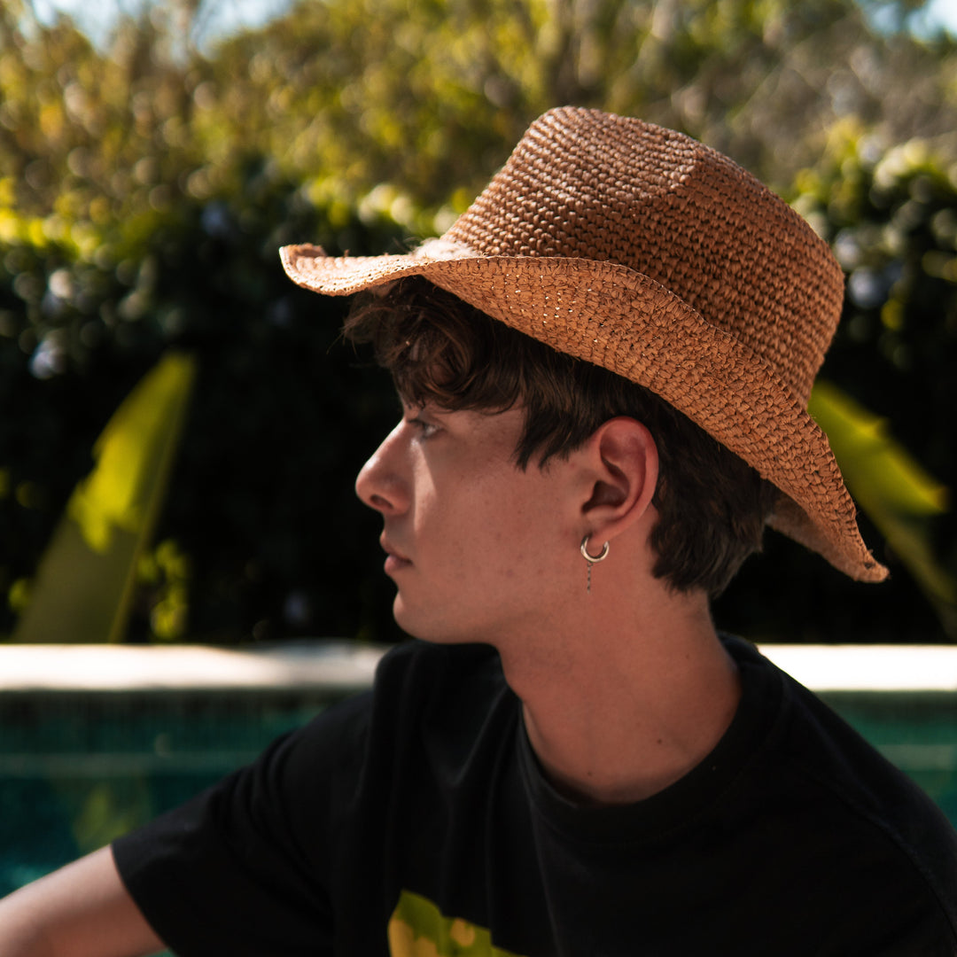 Person wearing a straw hat sitting outdoors with greenery in the background